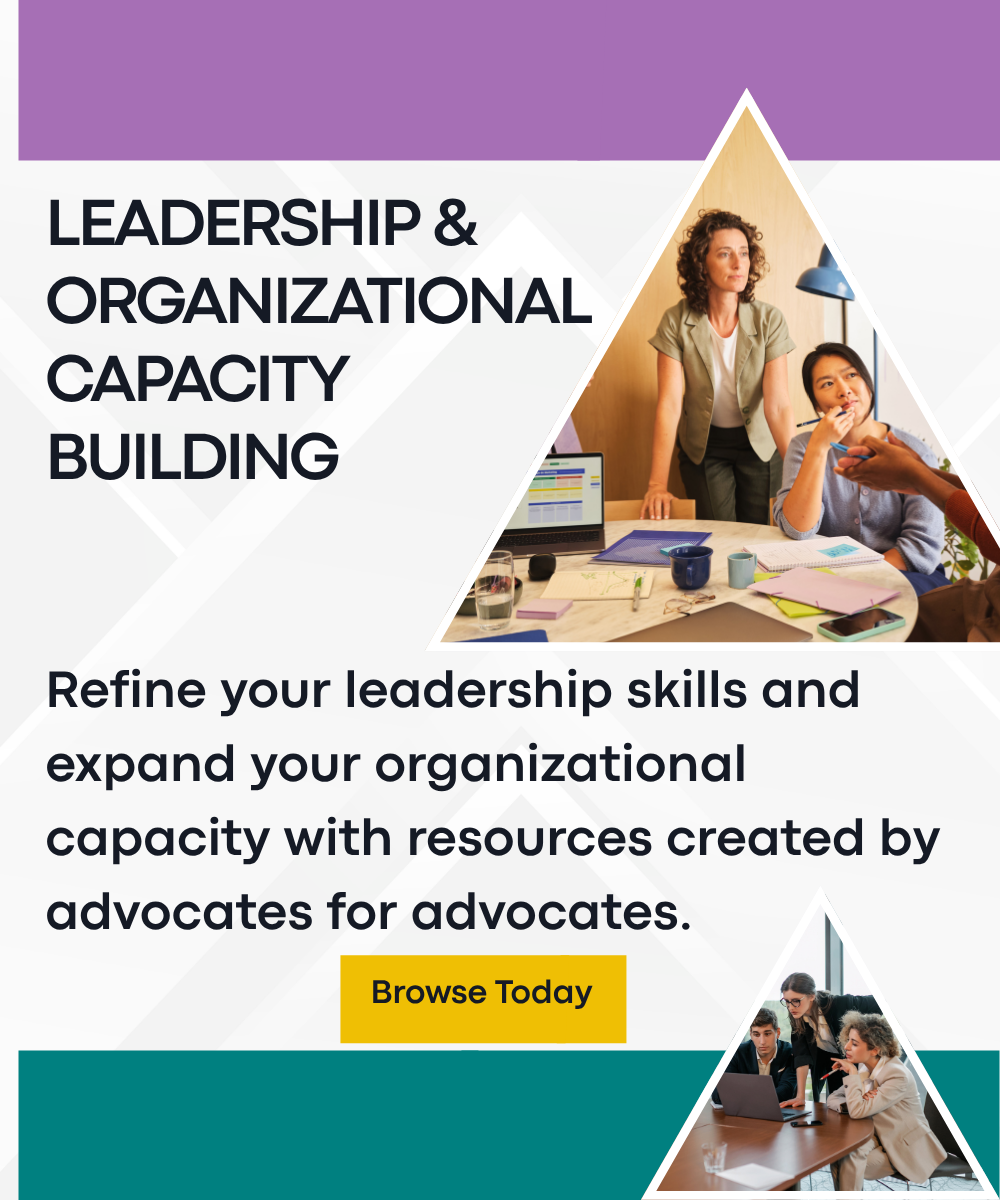 One woman standing and one woman sitting at a table listening to a peer give a presentation